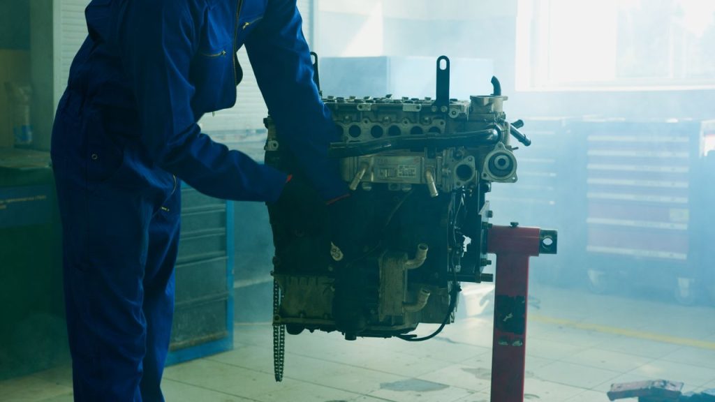 mechanic-fixing-an-engine-8985465 Mechanic in blue overalls inspecting an engine in an indoor garage.
