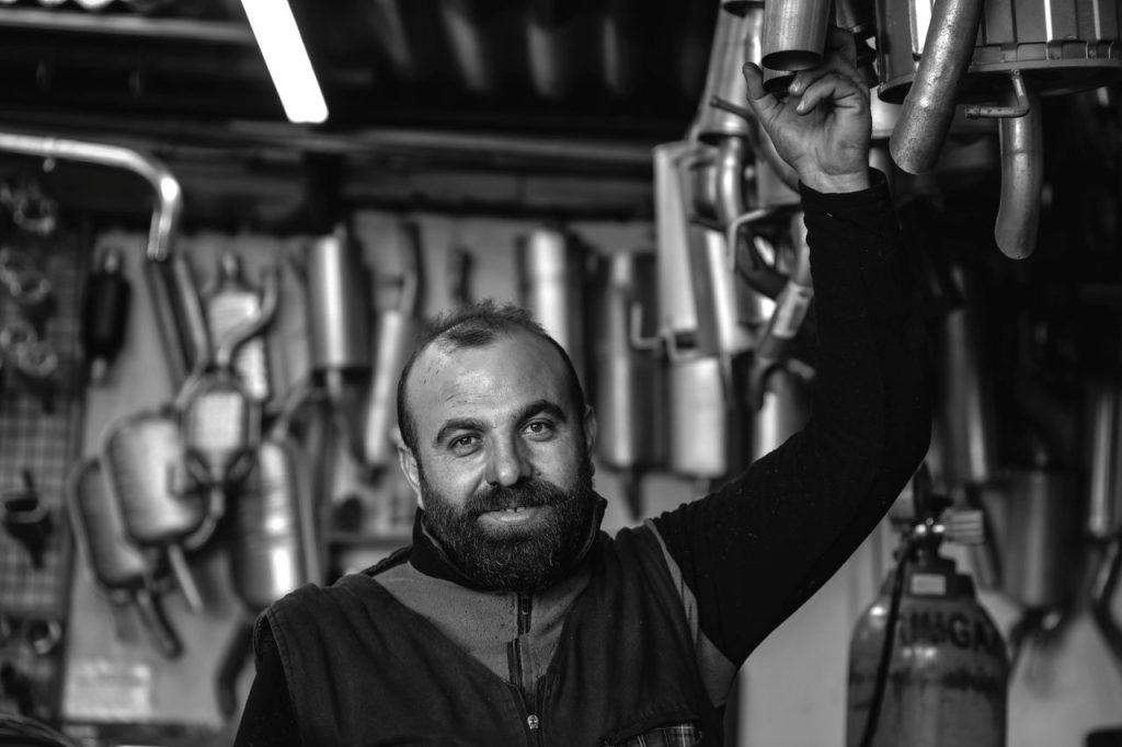 smiling-mechanic-in-car-repair-garage-34011409 A smiling mechanic holding an exhaust pipe in a car repair garage. Black and white photo.
